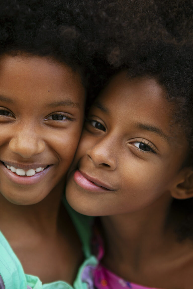 Close-up of two Black girls with natural hair, smiling cheek-to-cheek — a soft portrait of joy and sisterhood.